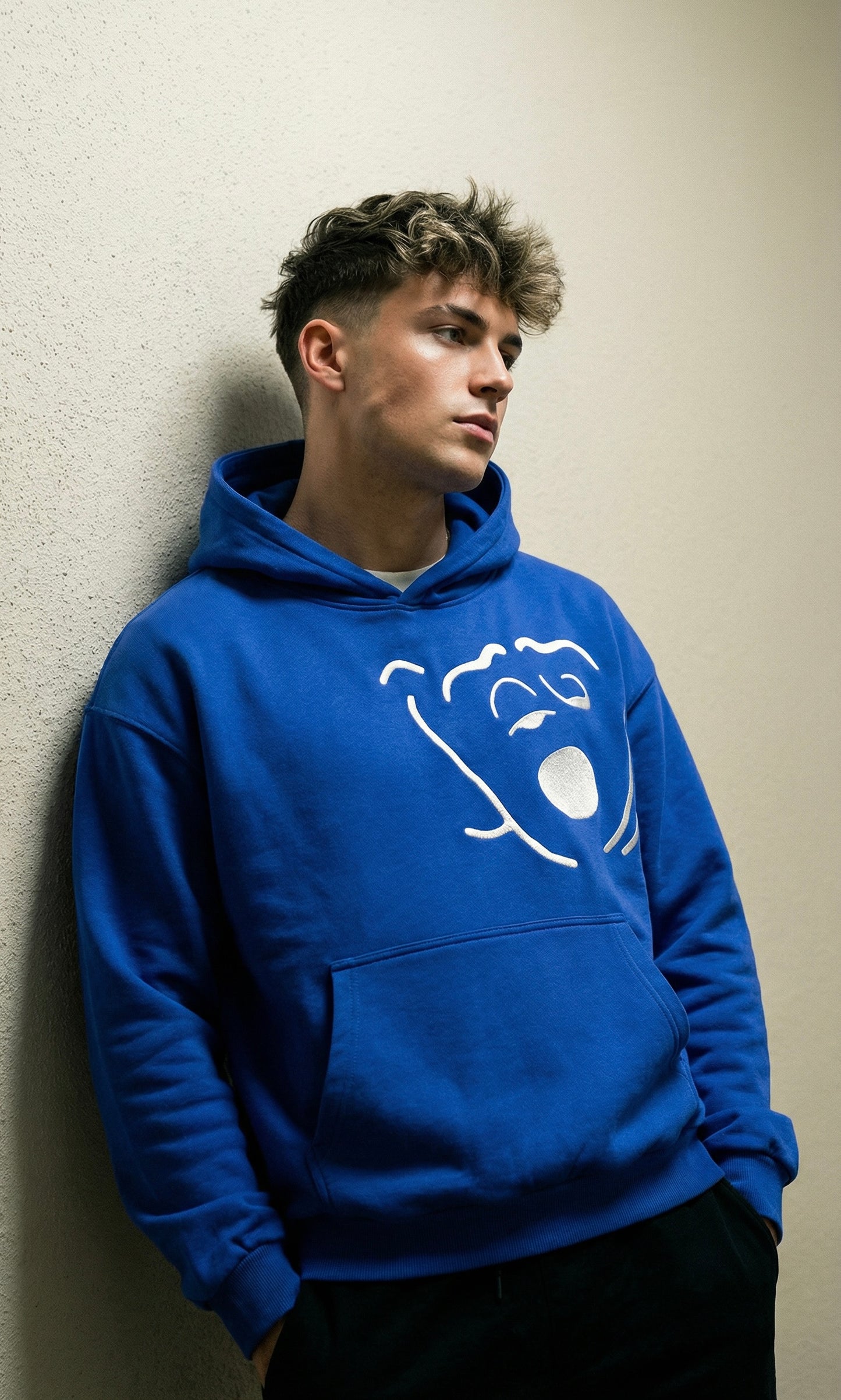 Person wearing a blue hoodie with a logo against a beige wall