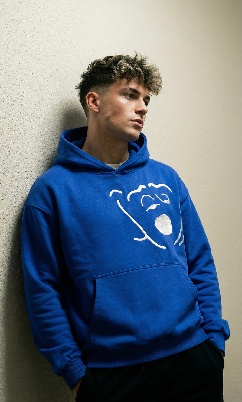 Person wearing a blue hoodie with a logo against a beige wall
