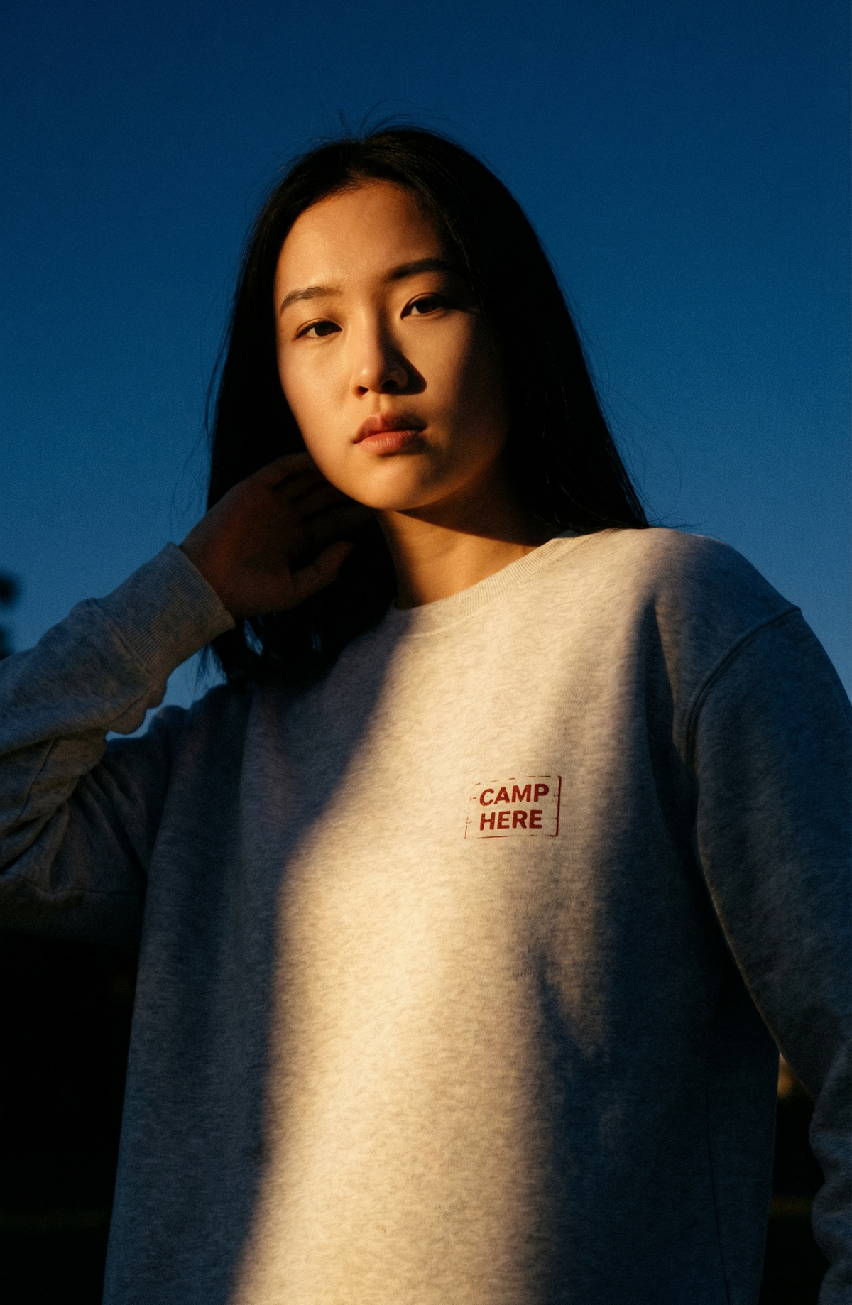 Person wearing a gray sweatshirt with 'CAMP HERE' text against a blue sky.