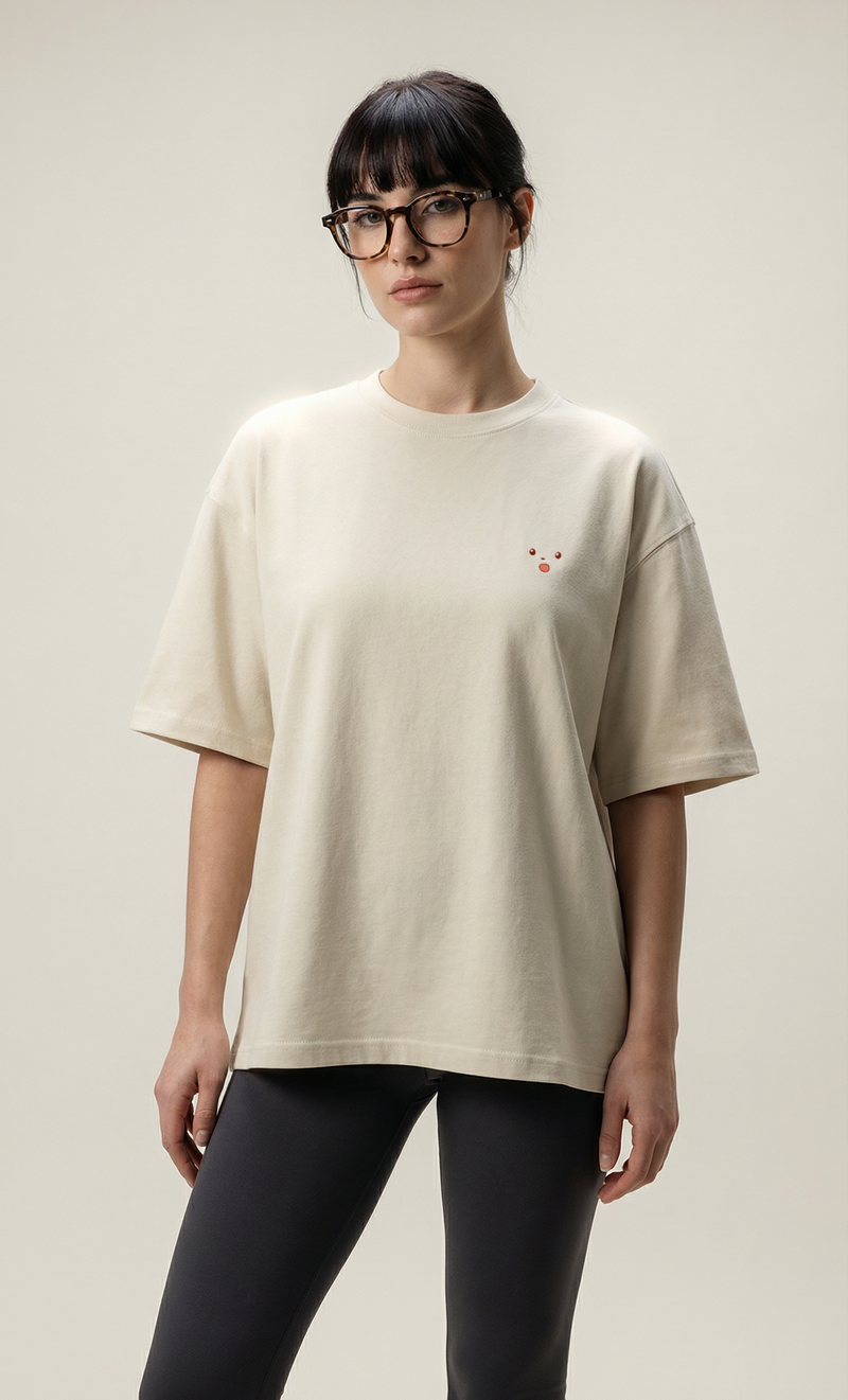 Person wearing a beige t-shirt with a small red graphic on a plain background